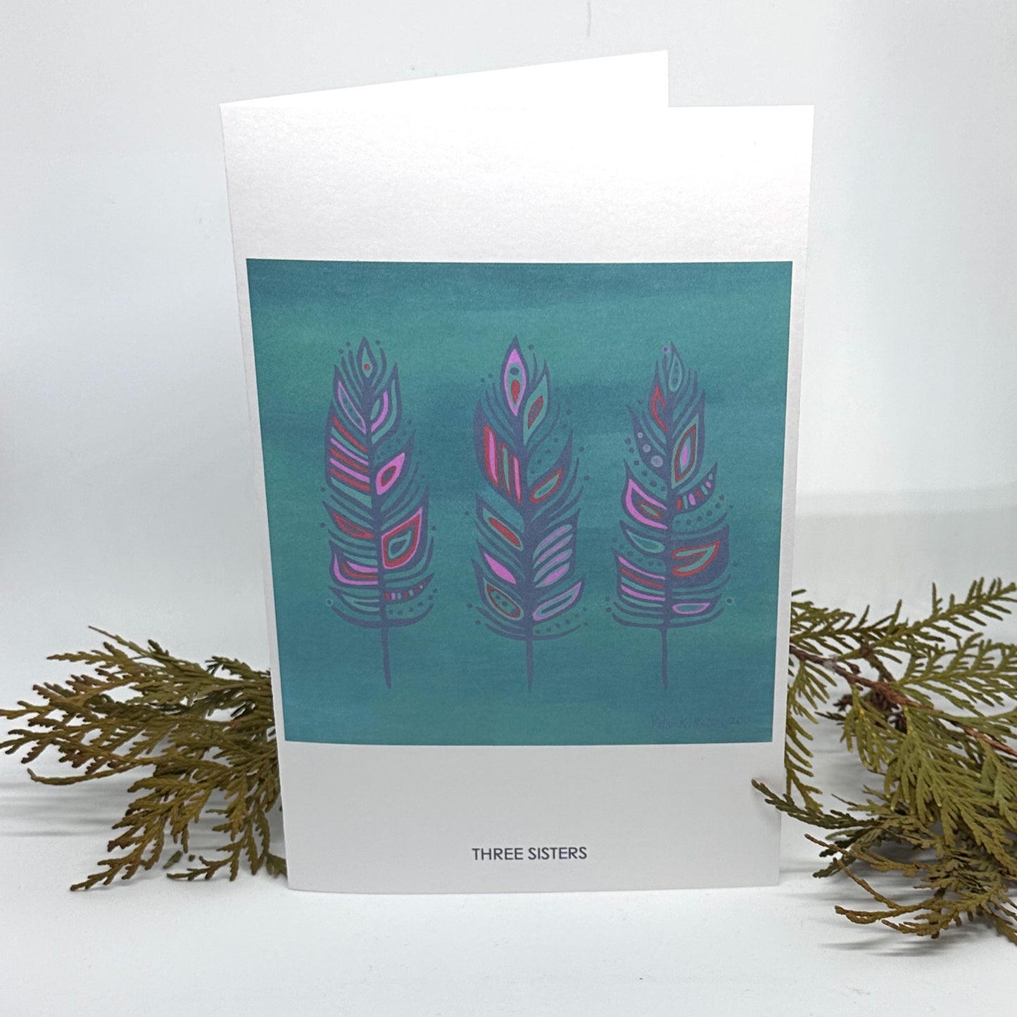 Patrick Hunter's original painting, Three Sisters, as a greeting card, standing open and framed by cedar boughs.