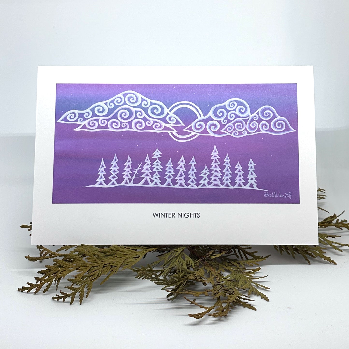 Patrick's painting of winter nights in woodland art style as a greeting card resting on cedar boughs.