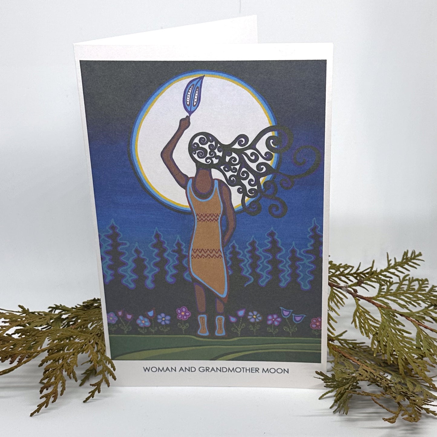 Patrick Hunter's painting, Woman and Grandmother Moon, as a greeting card standing open and framed by cedar boughs.