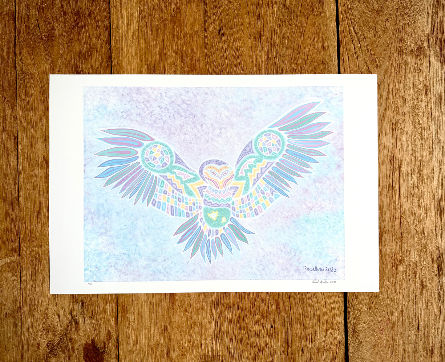 Patrick's print of original woodland art style owl with outstretched wings on white paper, against a wood grain background.