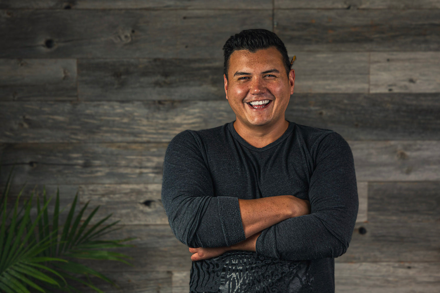 Image of Patrick Hunter, smiling with arms folded and a paintbrush behind the left ear in front of a wood panel background.