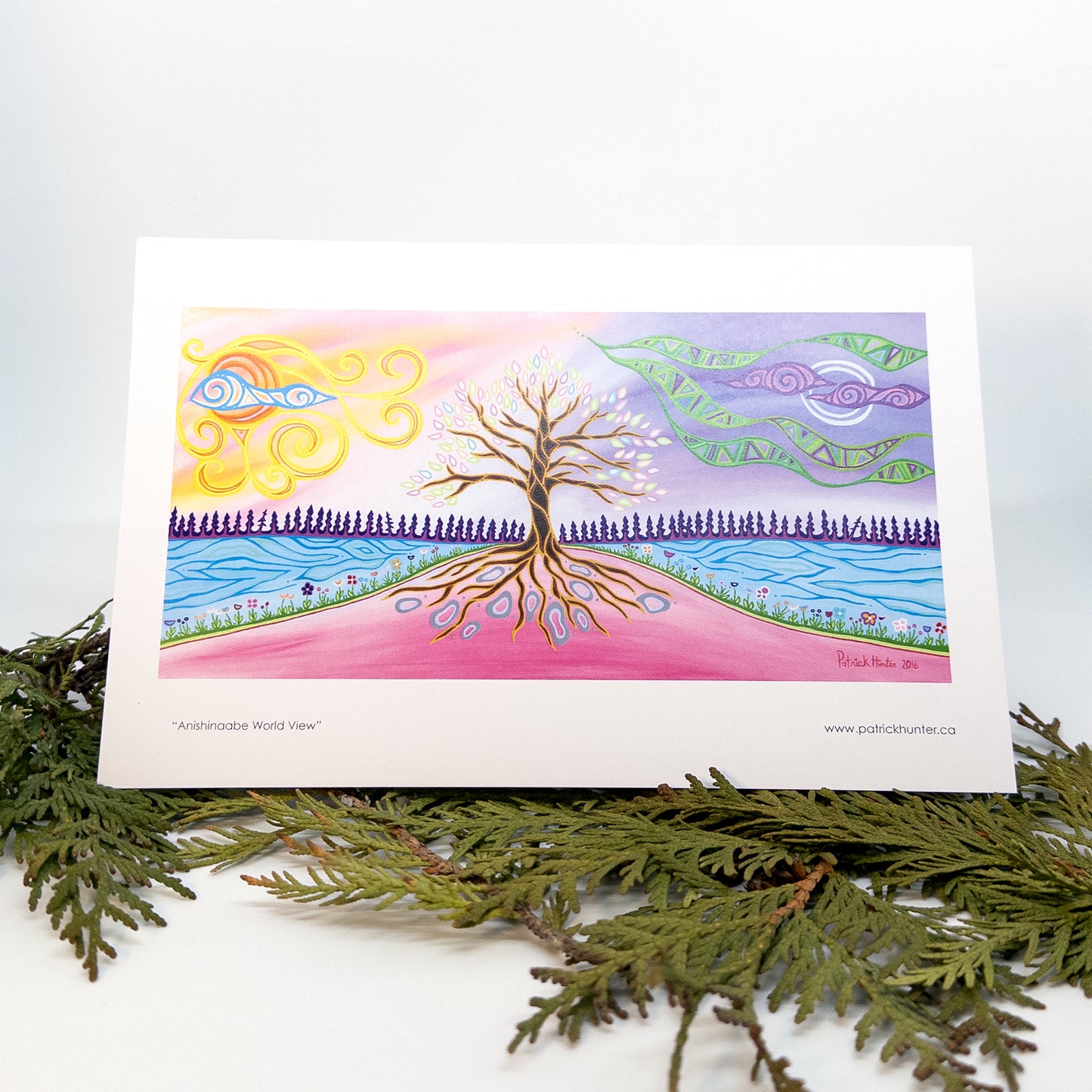 A greeting card with Patrick Hunter's Anishinaabe World View painting in woodland art style is displayed on some cedar boughs.