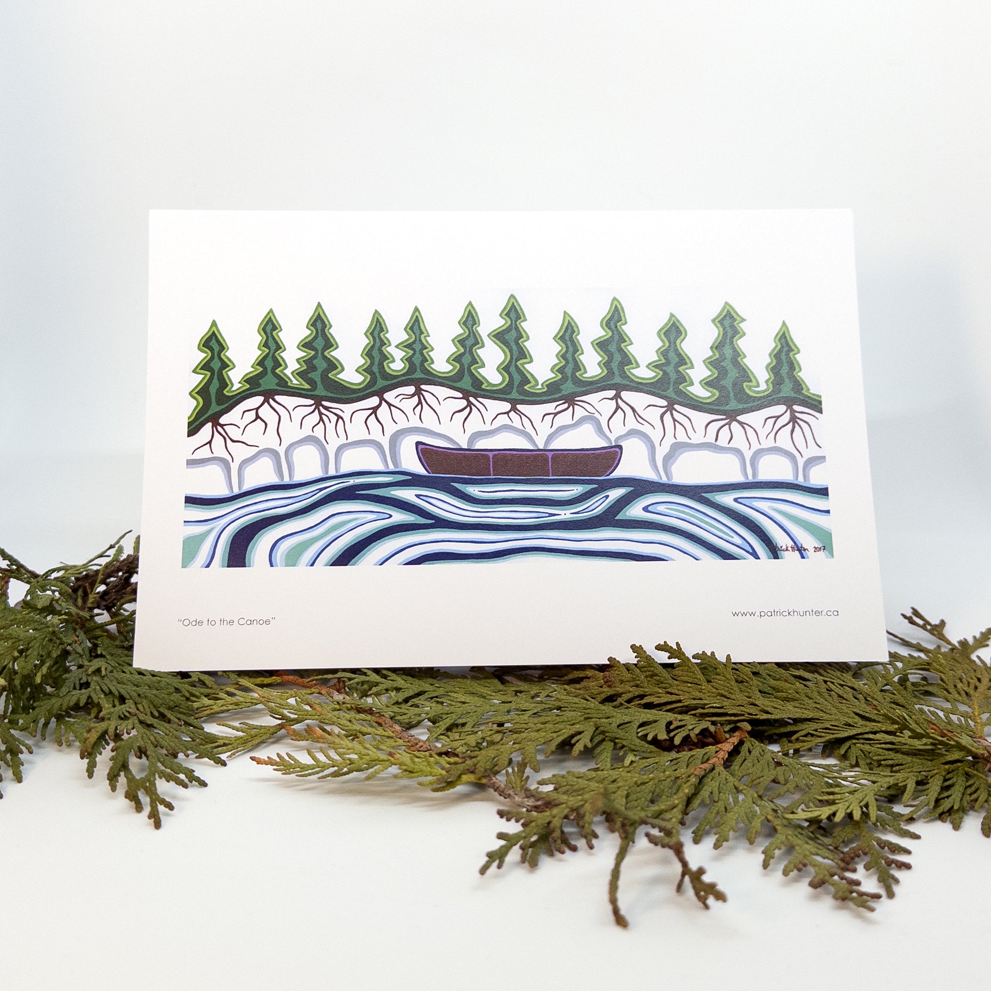 Patrick's painting, Ode to the Canoe, in woodland art style, as a greeting card that stands up over boughs of cedar