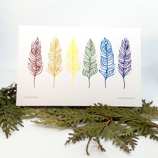 Patrick's painting of six eagle feathers in pride colours, in woodland art style, as a greeting card propped up over boughs of cedar.