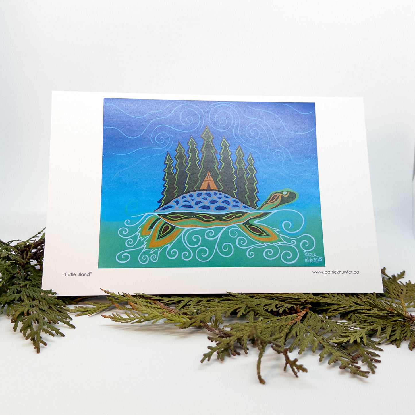 Patrick's painting of Turtle Island in woodland art style as a greeting card standing open on cedar boughs.