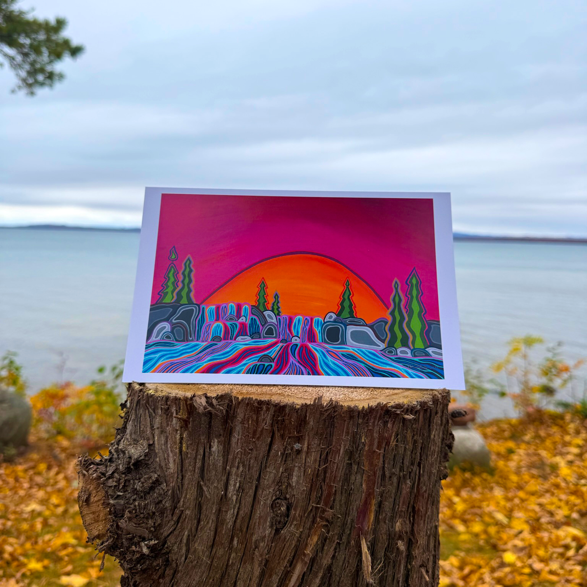 A greeting card with Patrick's woodland art style painting of cascading waterfalls against a setting sun and vibrant background.