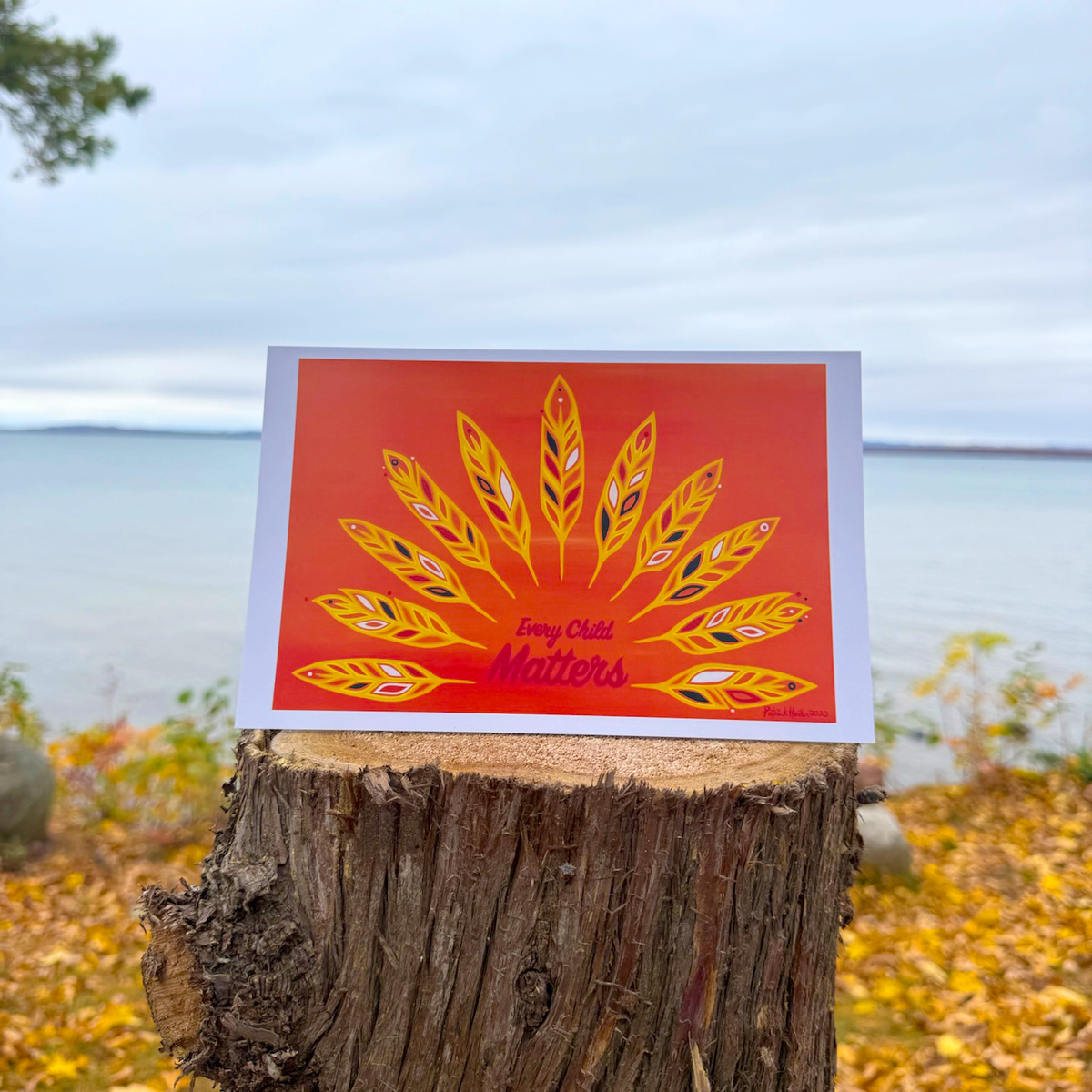 A greeting card of Patrick's woodland art style painting of 11 feathers in a semi-circle around text that reads Every Child Matters, with oranges and yellows and reds being the predominant colours.