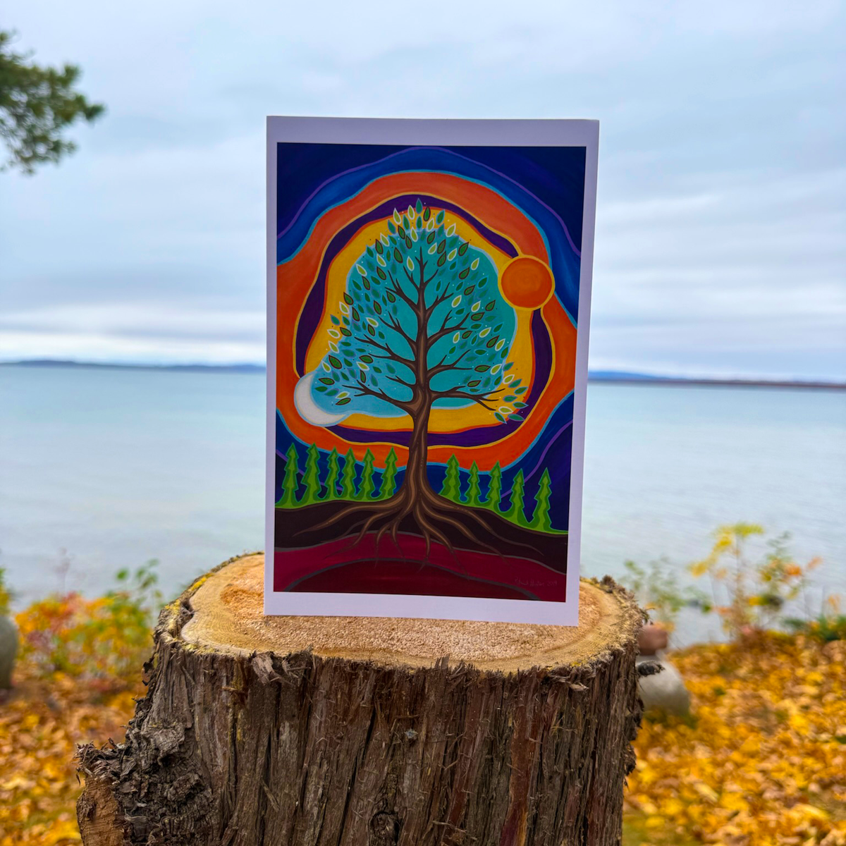 A greeting card with Patrick's woodland art style painting of a tree in balance with sun and moon, against a vibrant background.