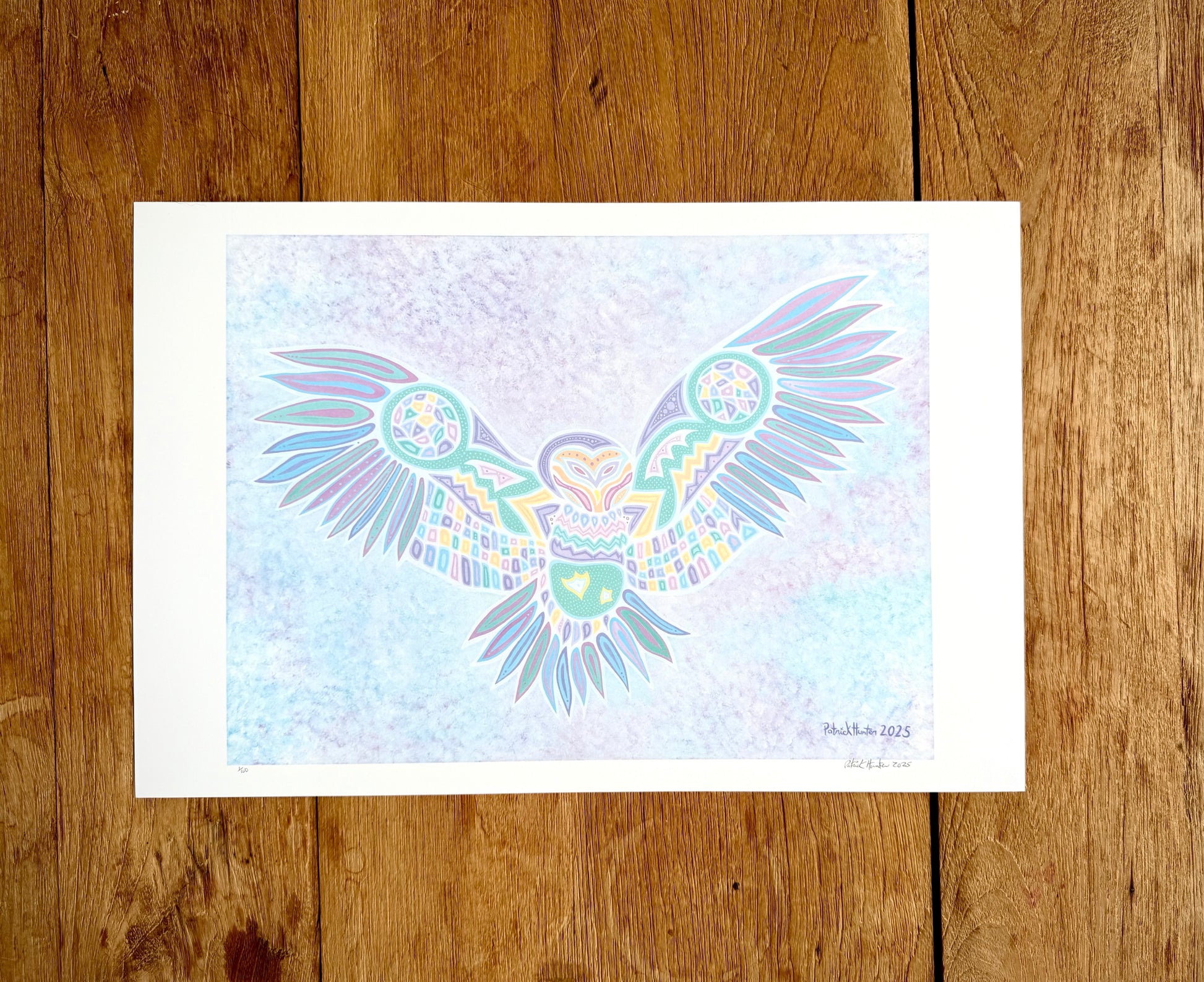 Patrick's print of original woodland art style owl with outstretched wings on white paper, against a wood grain background.