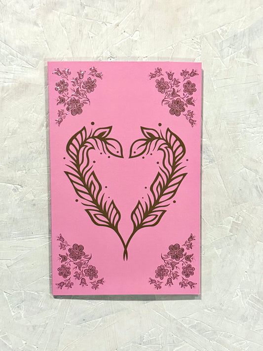 Patrick's woodland art style design of two feathers in the shape of a heart with floral embellishments in the four corners of the card. The card contains raised rose gold foil elements, over a bubble gum pink soft touch laminate coating.