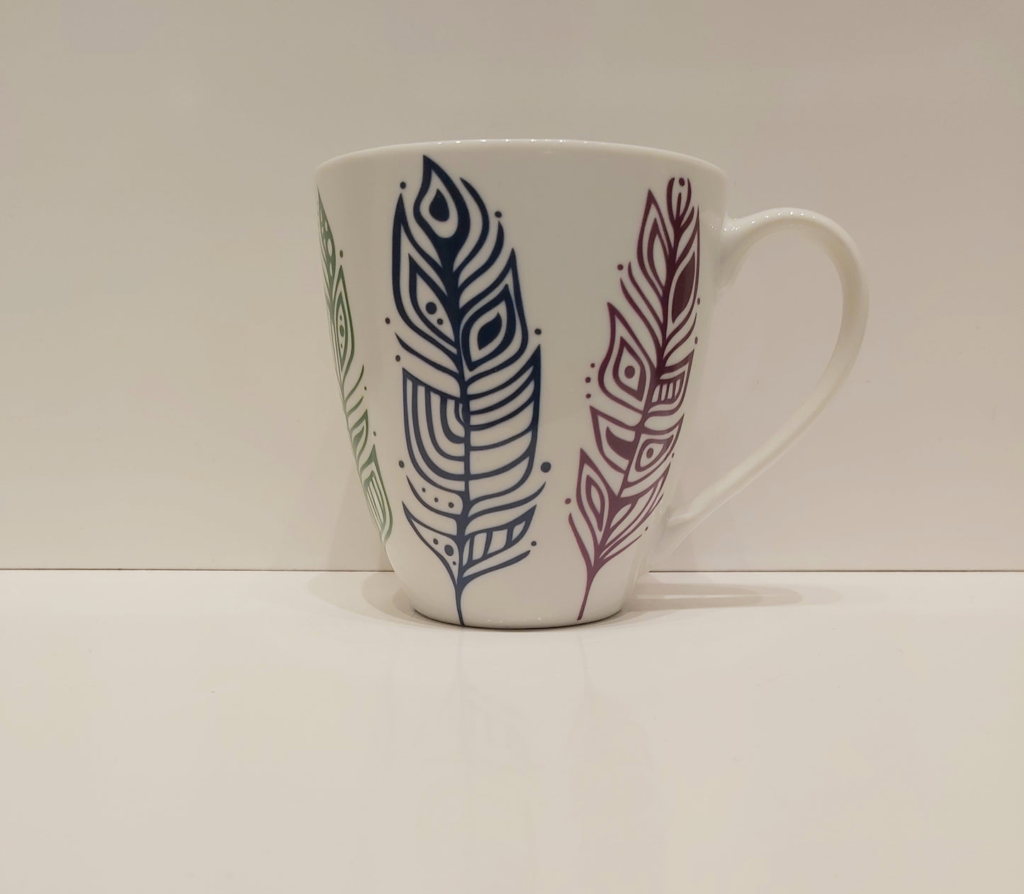 Patrick's Pride Feathers on a tall white mug against a neutral background.